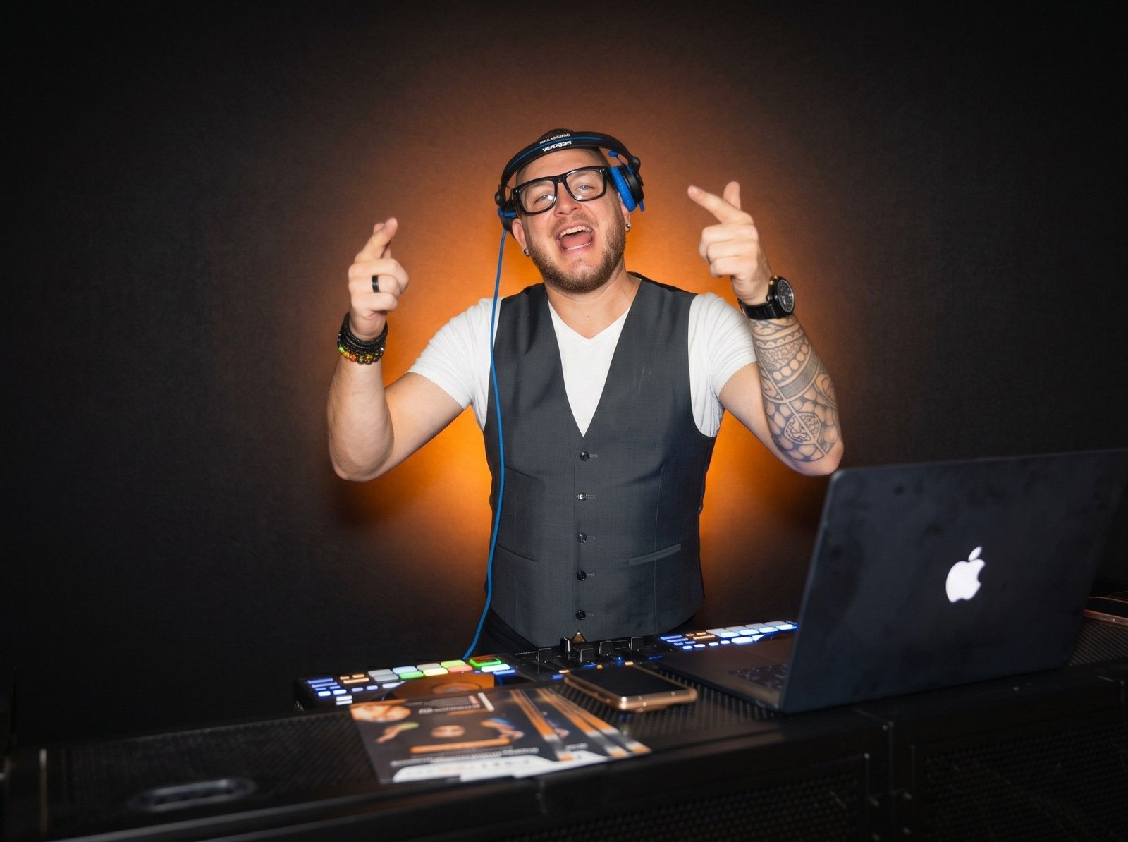 Joël R'Key au casque derrière sa table de mixage, tout sourire, devant un halo de lumière orange